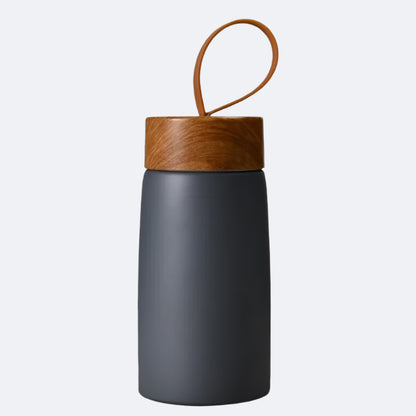 A grey-colored cylindrical bottle with a wooden lid and a carrying handle on top, possibly made of bamboo or a similar material.